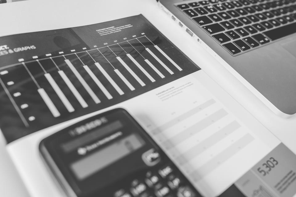 A calculator resting on printed financial reports with bar charts, next to a laptop