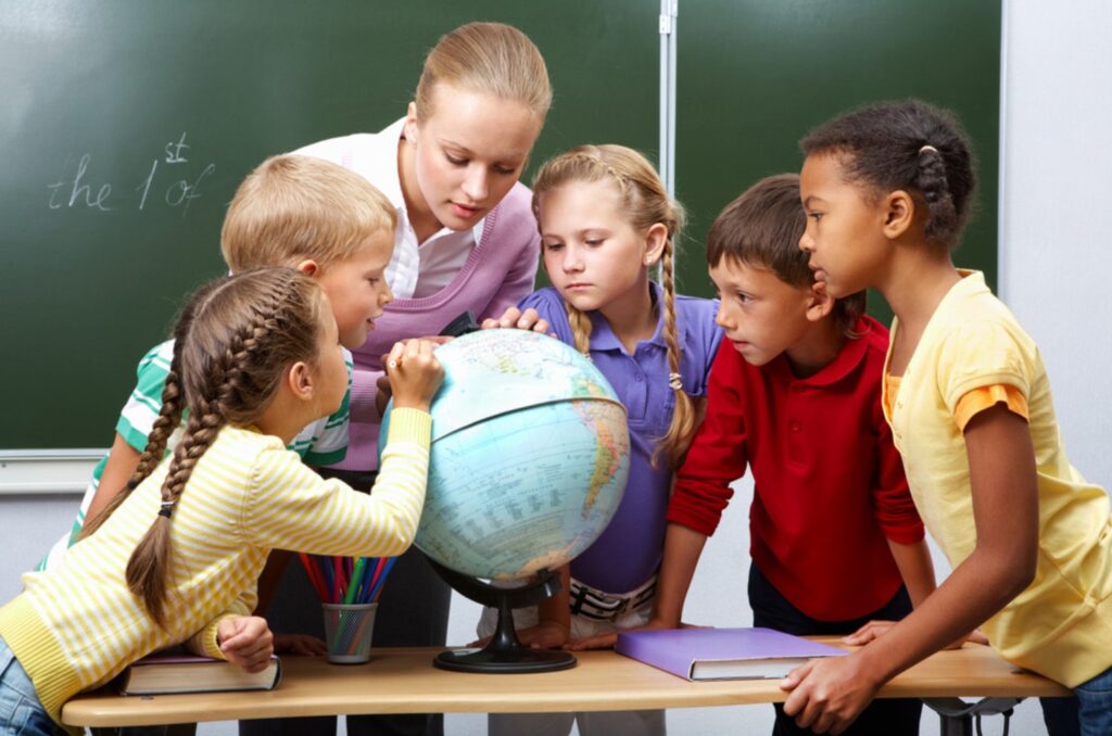 A teacher and a diverse group of public-school students gather around a globe in a classroom