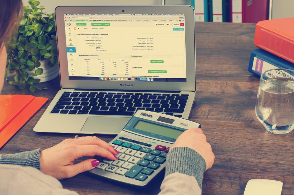 FundEDU | Tax Credit Scholarship Experts | What Families Actually Pay: A Free Worksheet for Counting Every School Cost A person at a laptop reviewing a spreadsheet while using a desktop calculator